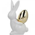 Floristik24 Conigli con uovo d&#39;oro, conigli in ceramica per Pasqua bianco nobile, dorato H13cm 2pz
